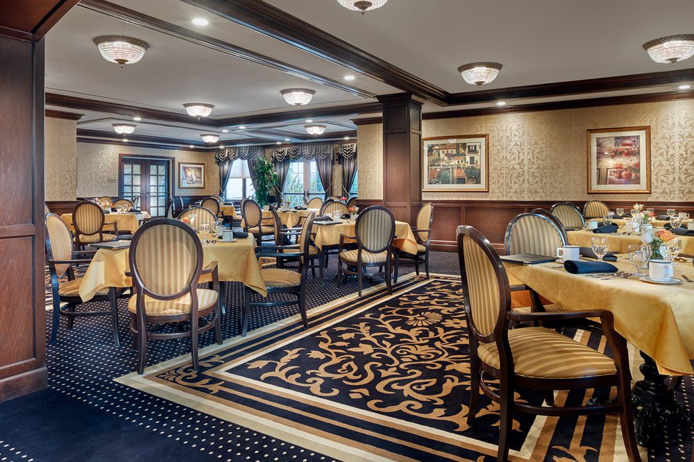 An elegant restaurant dining room with beautifully arranged tables and chairs, adorned with patterned carpet and tasteful lighting.