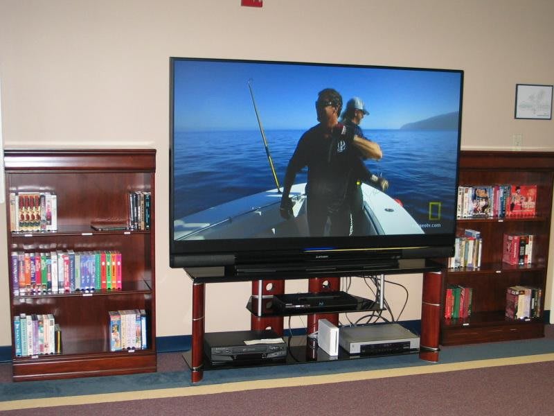 A flat-screen television displaying a fishing program, placed on an entertainment center flanked by bookshelves.