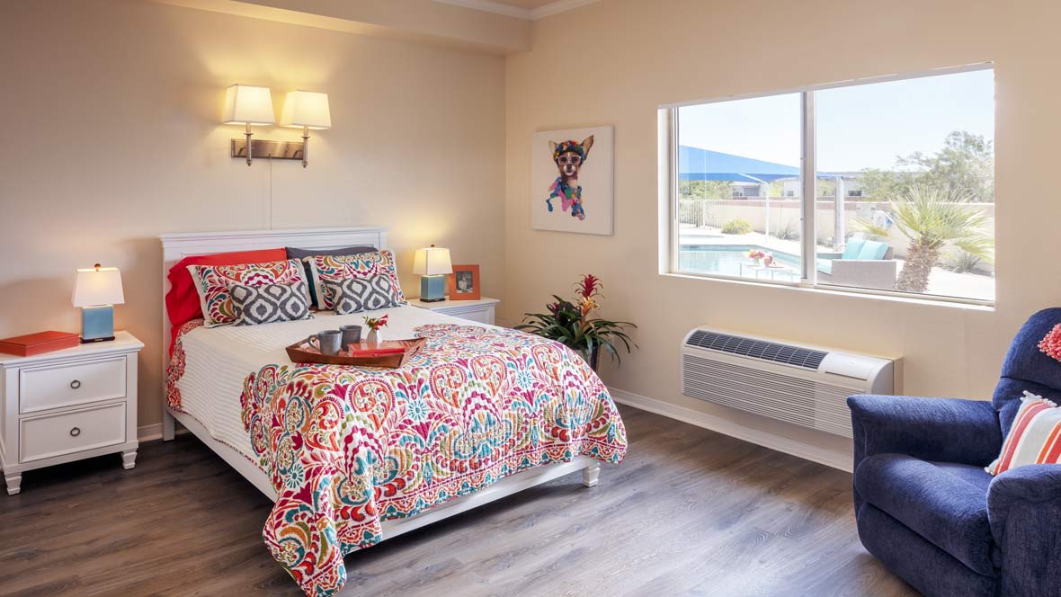A cozy bedroom with colorful bedding and natural light streaming in through a large window.