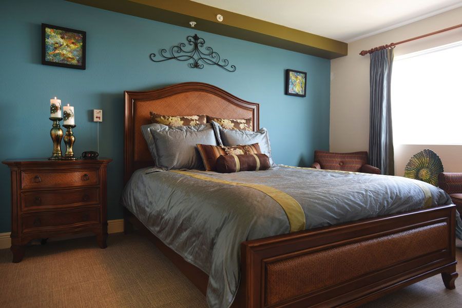 A cozy bedroom with a wooden bed frame against a blue accent wall, adorned with decorative pillows and artwork.