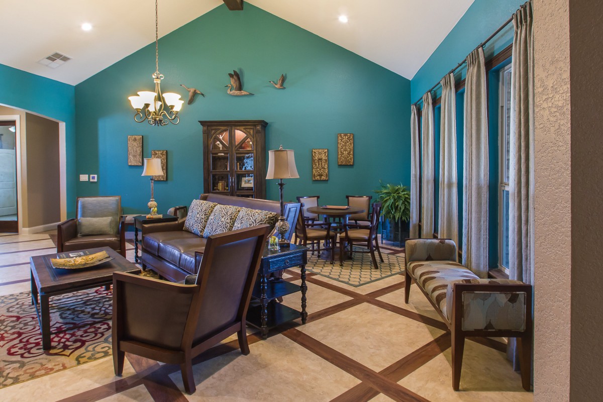 A cozy living room with teal walls, featuring elegant furniture and a dining area under a vaulted ceiling.