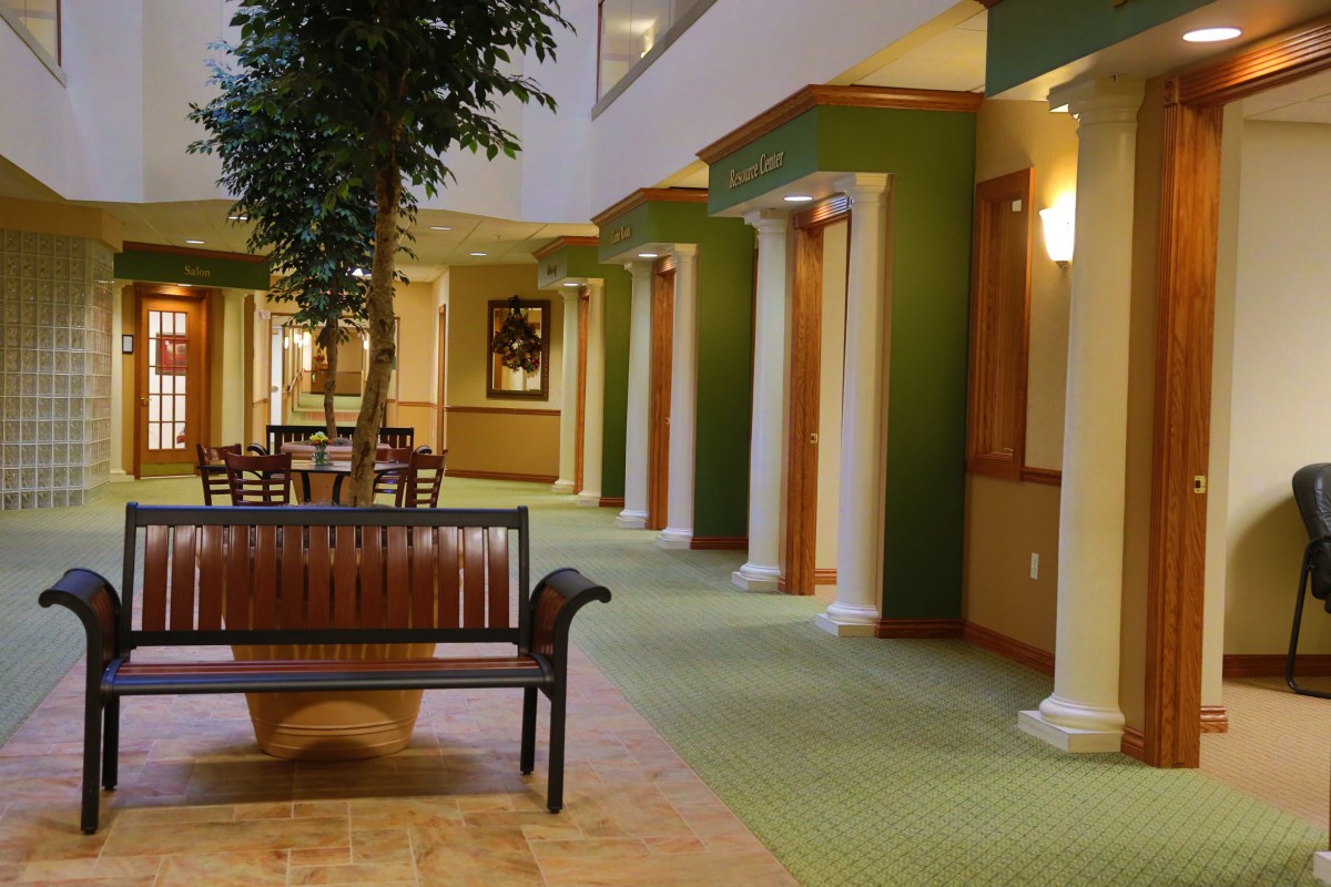 A spacious hallway featuring columns, green walls, a wooden bench, and artwork on display.