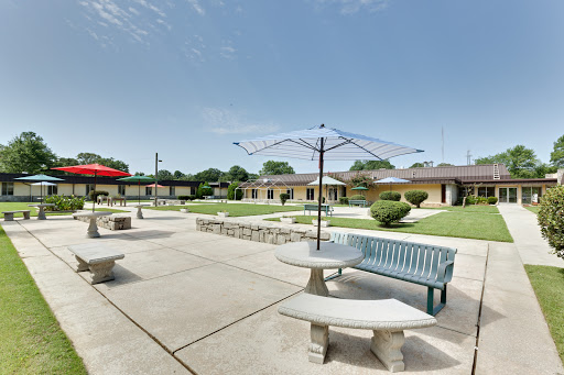 A serene outdoor courtyard featuring tables, benches, and lush landscaping under a clear blue sky.