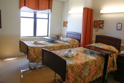 A spacious hospital patient room with two beds, featuring colorful bedding and natural light from the window.