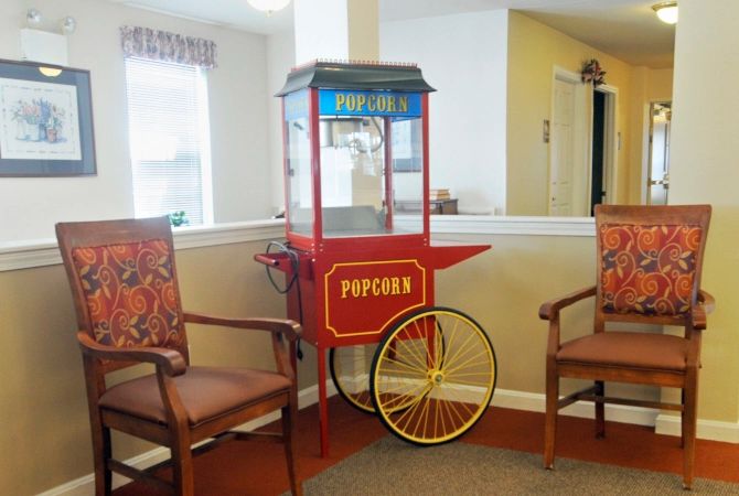 A vintage-style popcorn machine is placed between two chairs in a cozy indoor setting.