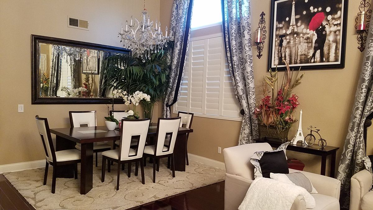 An elegant dining room with a chandelier, mirror, and stylish curtains.