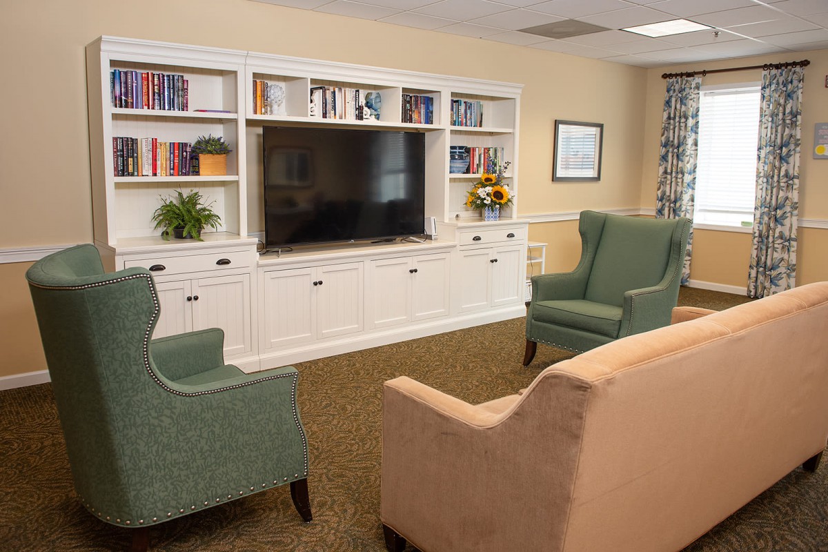 A cozy living room with a TV, bookshelves, and comfortable seating.