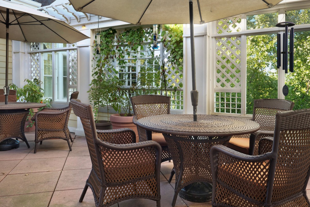 A tranquil outdoor patio with wicker furniture and umbrellas, surrounded by lush greenery.