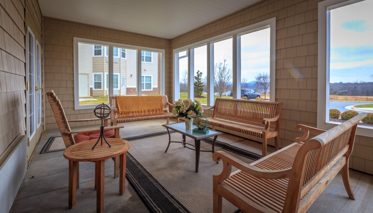 A cozy sunroom with wooden benches and a glass table surrounded by large windows.