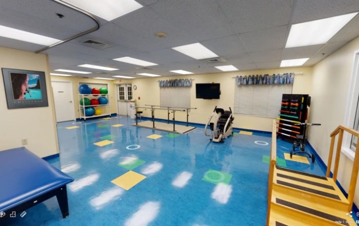 A well-lit physical therapy room with various exercise equipment and colorful gym mats.