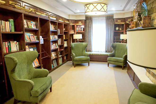 A cozy library reading room with green armchairs and bookshelves lining the walls.