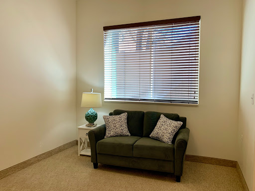 A cozy corner in a living room featuring a green sofa, decorative pillows, and a lamp beside a window.