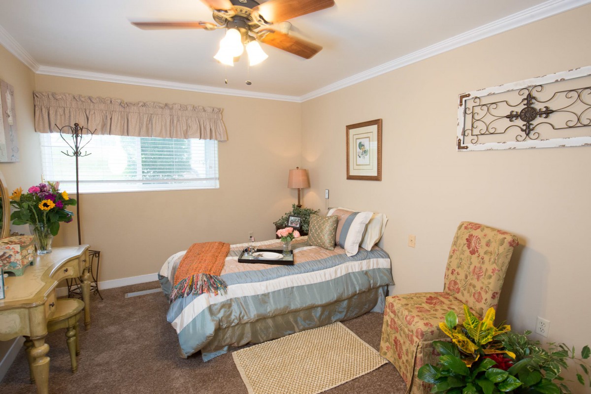 A cozy bedroom with a neatly made bed, ceiling fan, and warm lighting.
