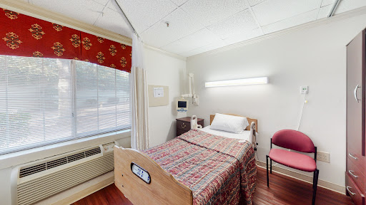 A cozy hospital patient room featuring a bed, window, and chair.