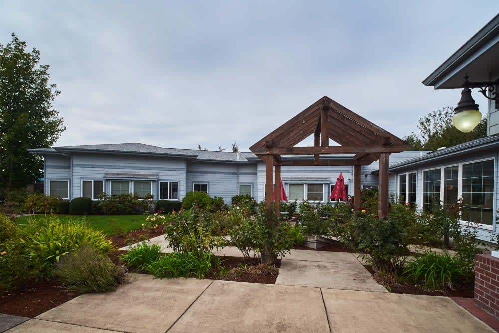 A peaceful garden with a wooden archway leading to a building in the background.