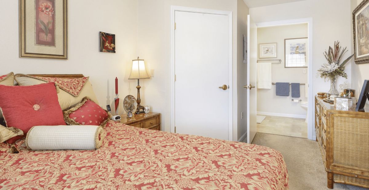 A cozy bedroom with a patterned blanket, nightstand, and a lamp near the door leading to a bathroom.