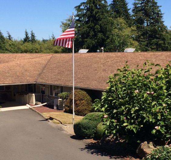 A building with an American flag in front, surrounded by greenery under a clear blue sky.