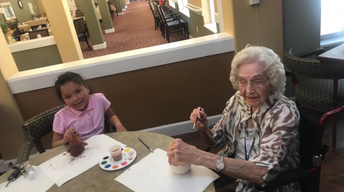 An elderly woman and a child enjoy painting together at a table indoors.