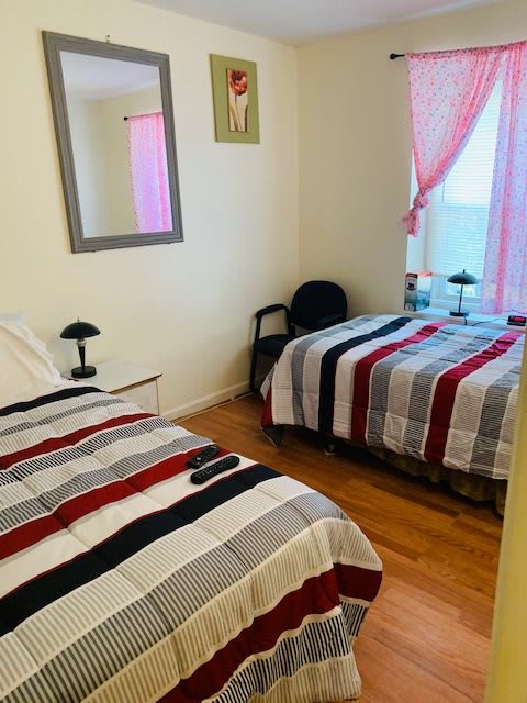 A cozy bedroom with two twin beds featuring striped bedding, a mirror on the wall, and a window with pink curtains.