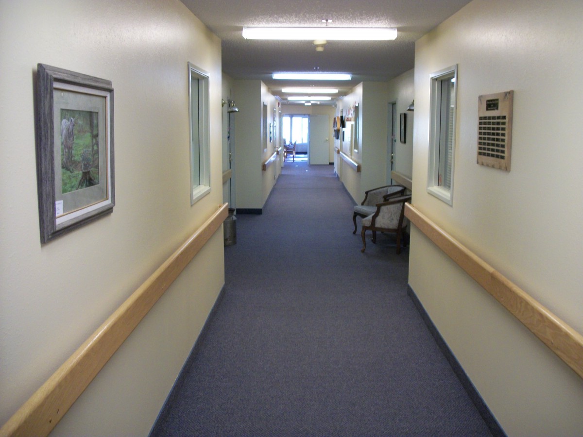 A long, clean hospital corridor with fluorescent lights and chairs along the walls.