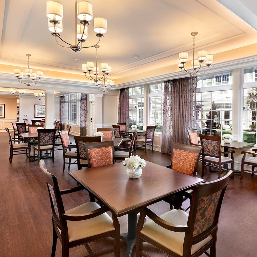A spacious and elegant dining area with multiple tables and chairs, featuring large windows and chandeliers.