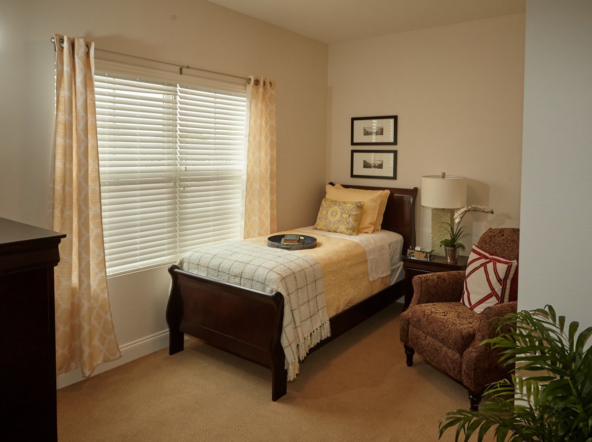 A cozy bedroom with a single bed, armchair, and window with curtains.