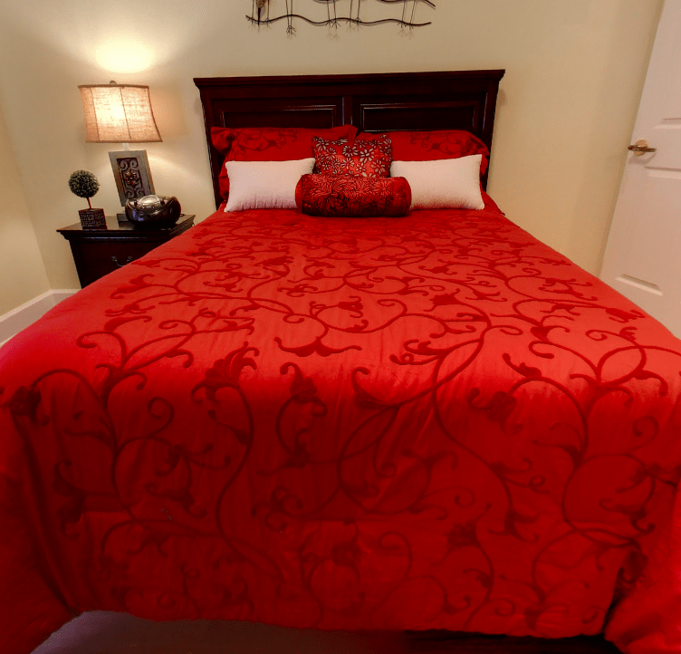 A cozy bedroom featuring a bed with a vibrant red bedspread and decorative pillows.