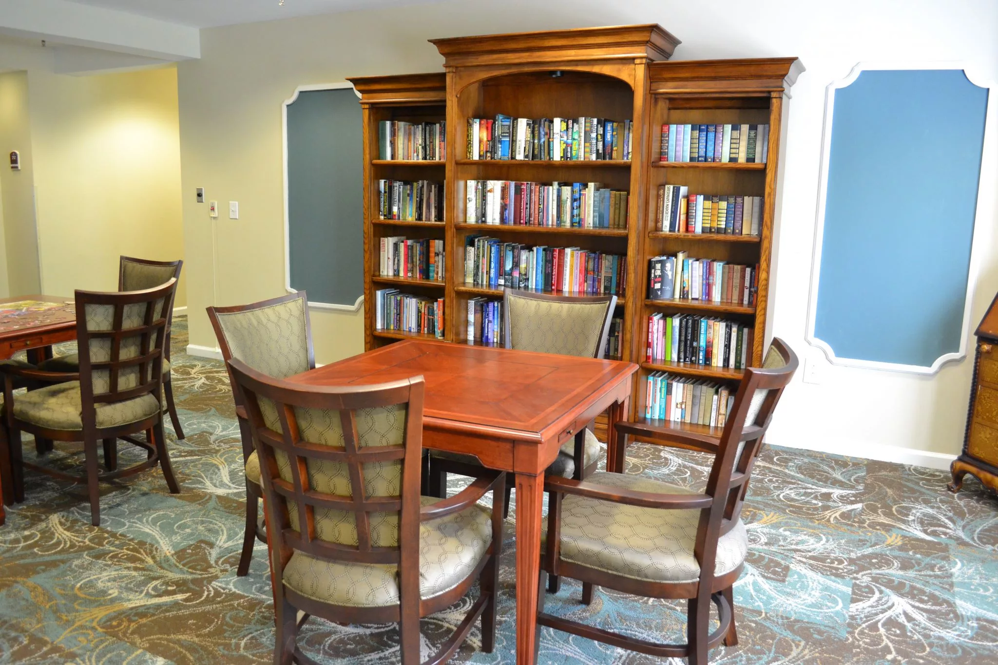 A cozy reading area with a wooden table and chairs surrounded by a large bookshelf filled with books.
