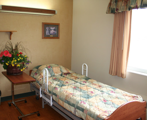 A cozy hospital room featuring a patient bed, a floral arrangement, and natural light from the window.