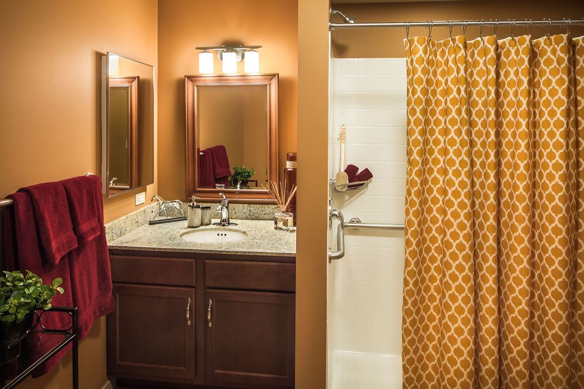 A cozy bathroom with warm lighting, featuring a marble countertop sink, a shower with a patterned curtain, and decorative elements.