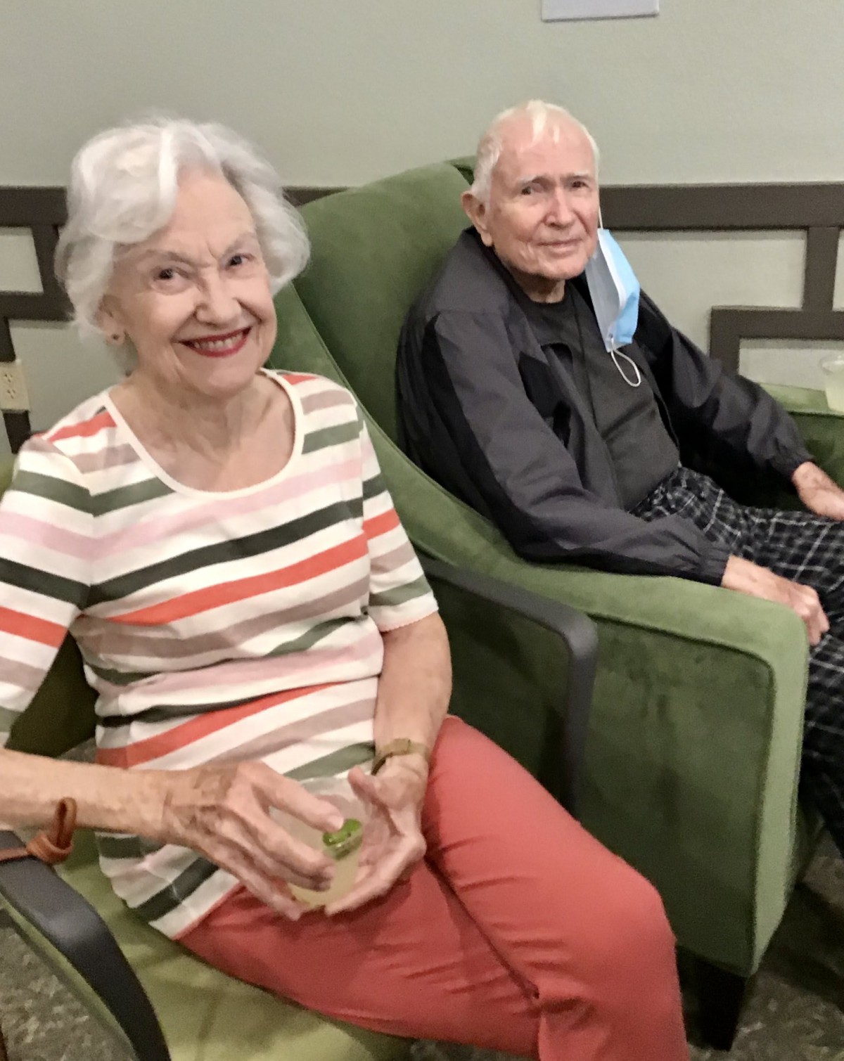 Two elderly individuals seated indoors, one smiling at the camera.