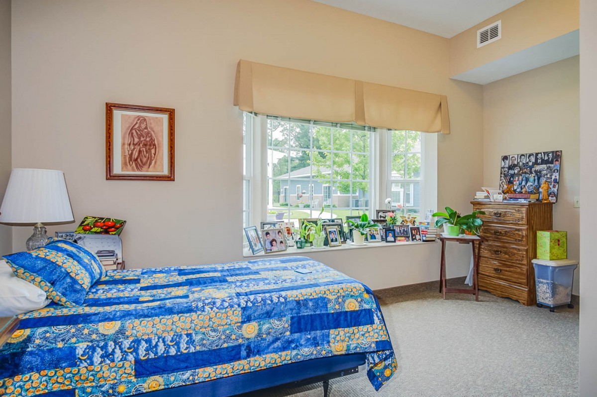 A cozy bedroom with a colorful quilt on the bed and sunlight streaming through a large window.