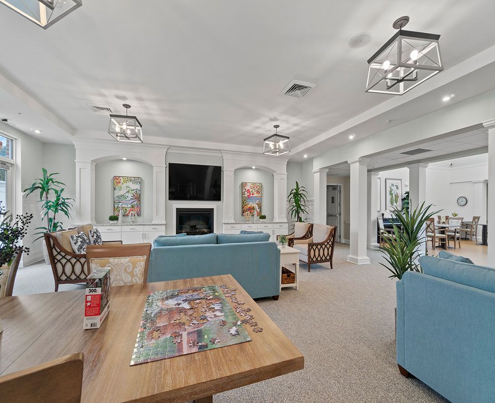 A modern living room with blue couches, a coffee table featuring a puzzle, and a fireplace beneath a mounted TV.
