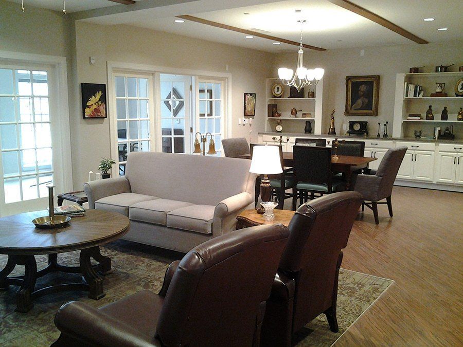A cozy and elegant living room with a connected dining area, featuring comfortable sofas, armchairs, and a chandelier.