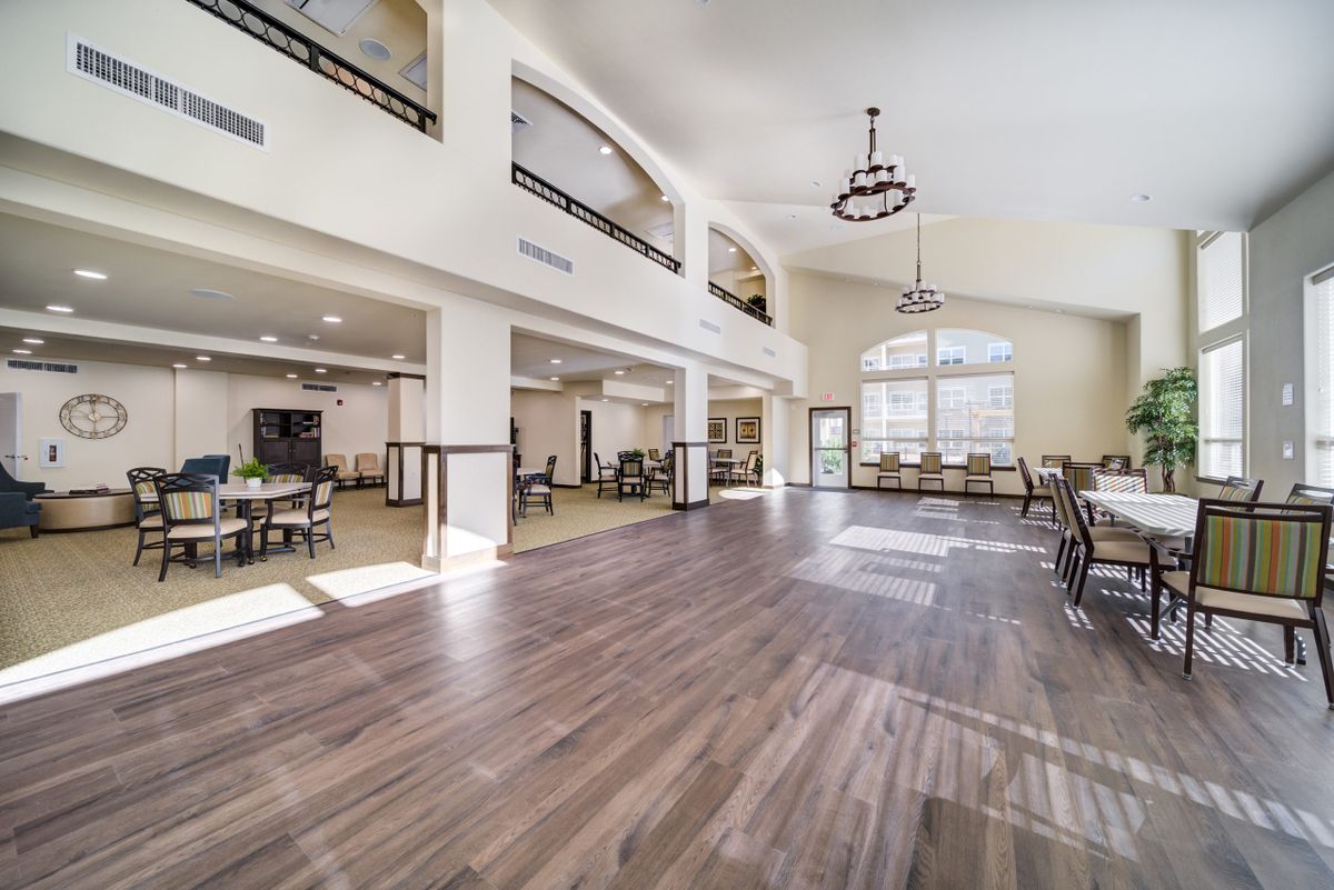 A spacious and modern interior featuring wooden flooring, high ceilings, large windows, and elegant chandeliers.