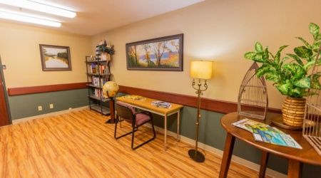 A small office corner with a desk, chair, lamp, and bookshelves on a wooden floor.