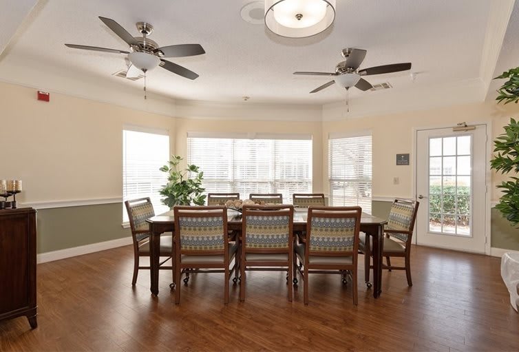 Spacious dining room with a large table and chairs, featuring ceiling fans and ample natural light from surrounding windows.
