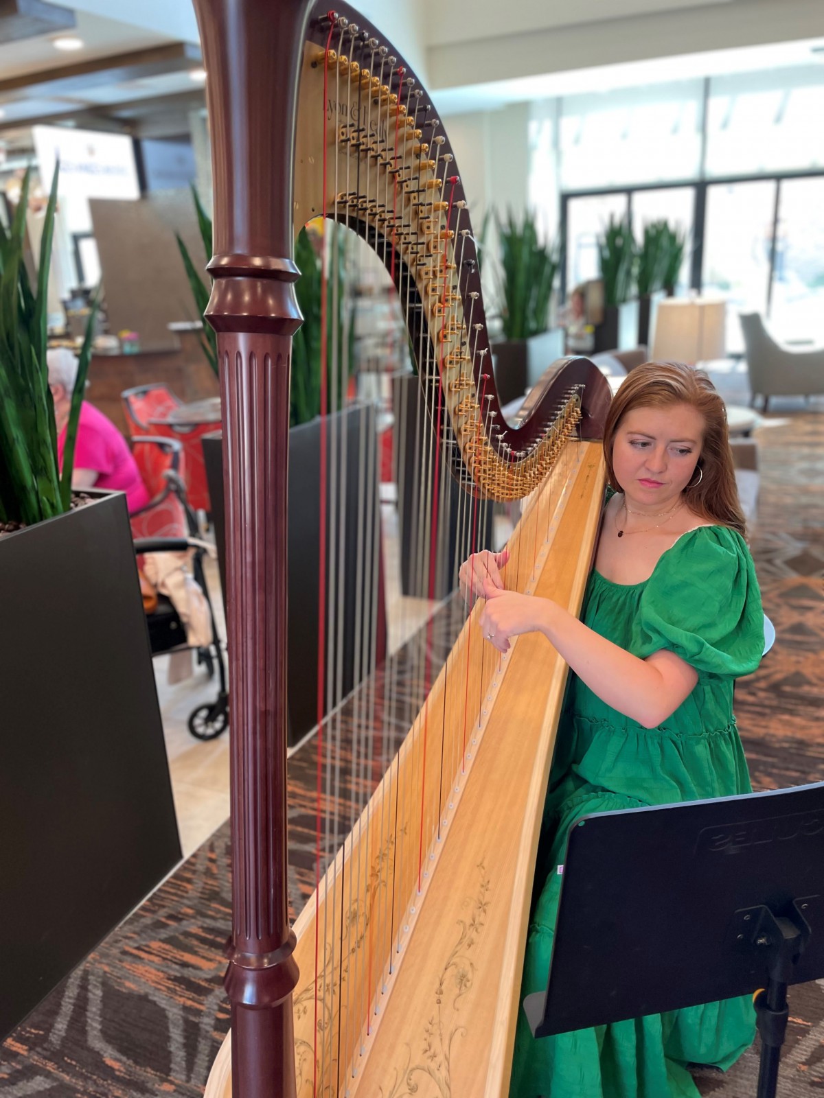A woman in a green dress playing the harp indoors.