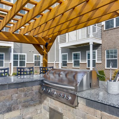 A stylish outdoor kitchen with a grill under a wooden pergola.