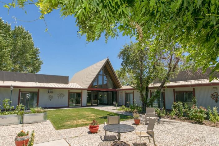 A modern house with a triangular roof surrounded by a spacious backyard and patio area.