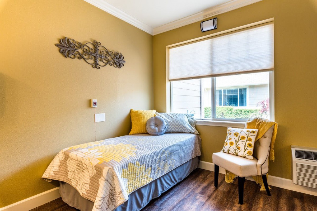 A cozy bedroom with a single bed, decorative pillows, and a chair next to a window.