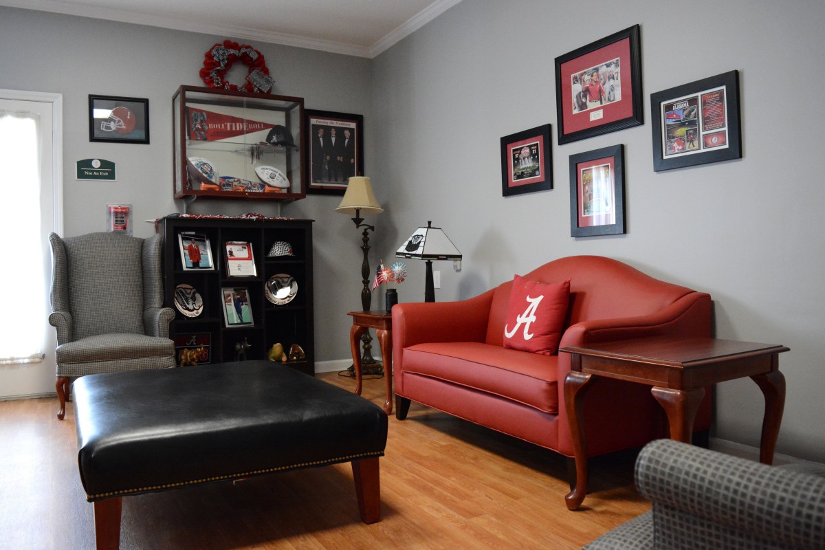 A cozy living room featuring sports-themed decor with a red couch, framed items on the wall, and hardwood floors.
