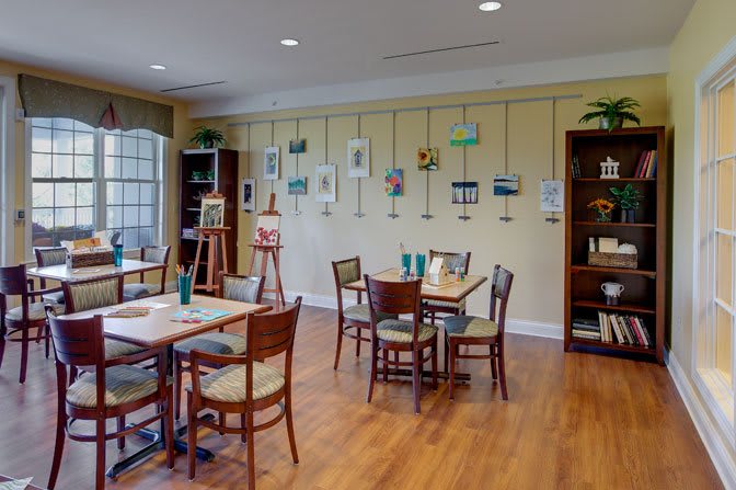 A cozy art studio with paintings displayed on the walls, tables and chairs arranged for activities, and easels set up for creating art.