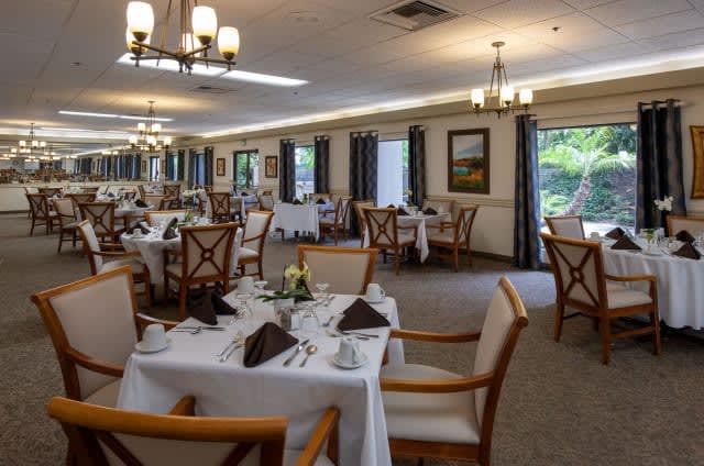 An elegant restaurant dining room with neatly arranged tables and chairs, set with white tablecloths and decorative place settings.