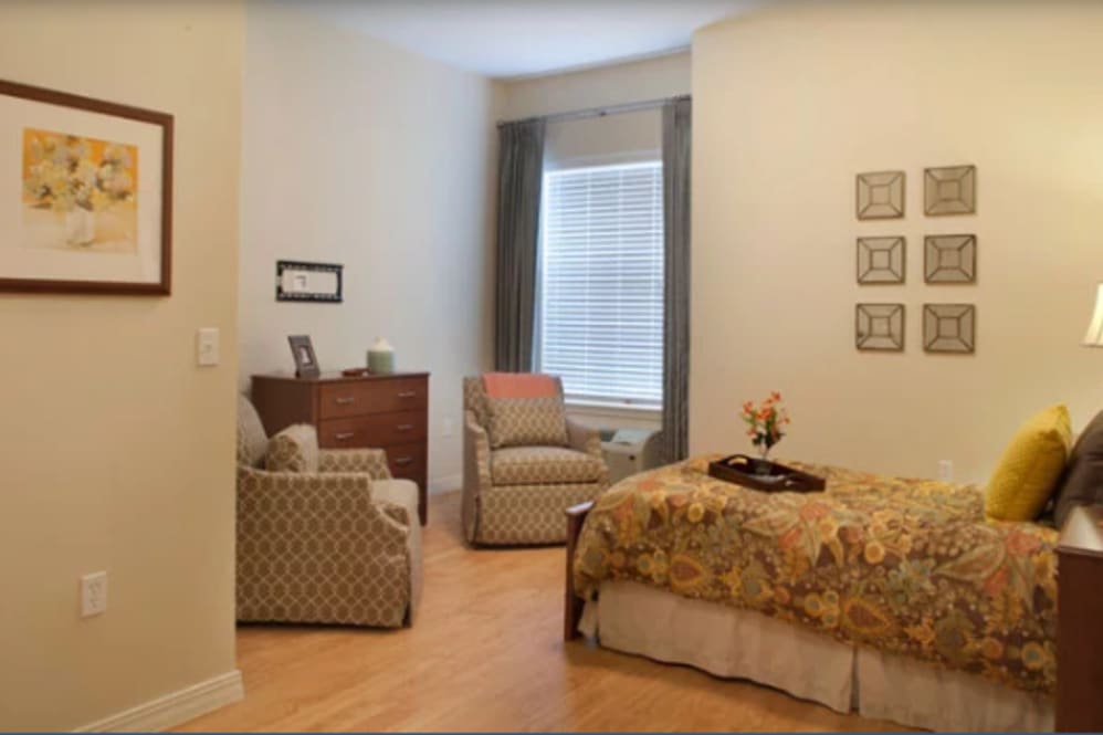 A cozy bedroom with a bed, chairs, and a window with curtains.