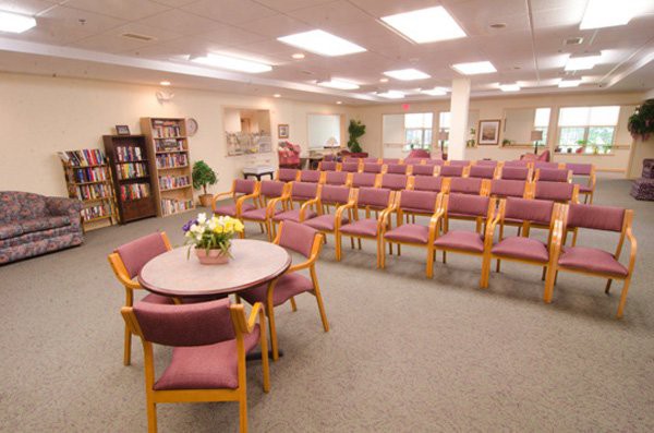 A spacious meeting room with rows of chairs and a small round table, surrounded by bookshelves and soft lighting.