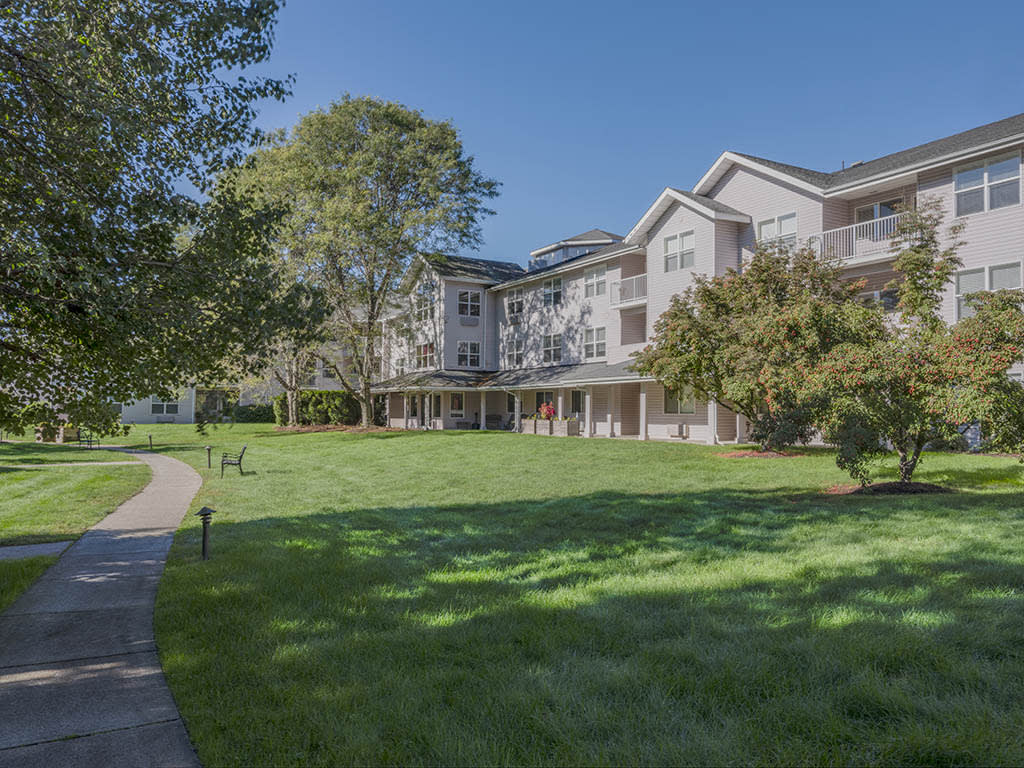 A residential building with a large lawn and trees under a clear blue sky.