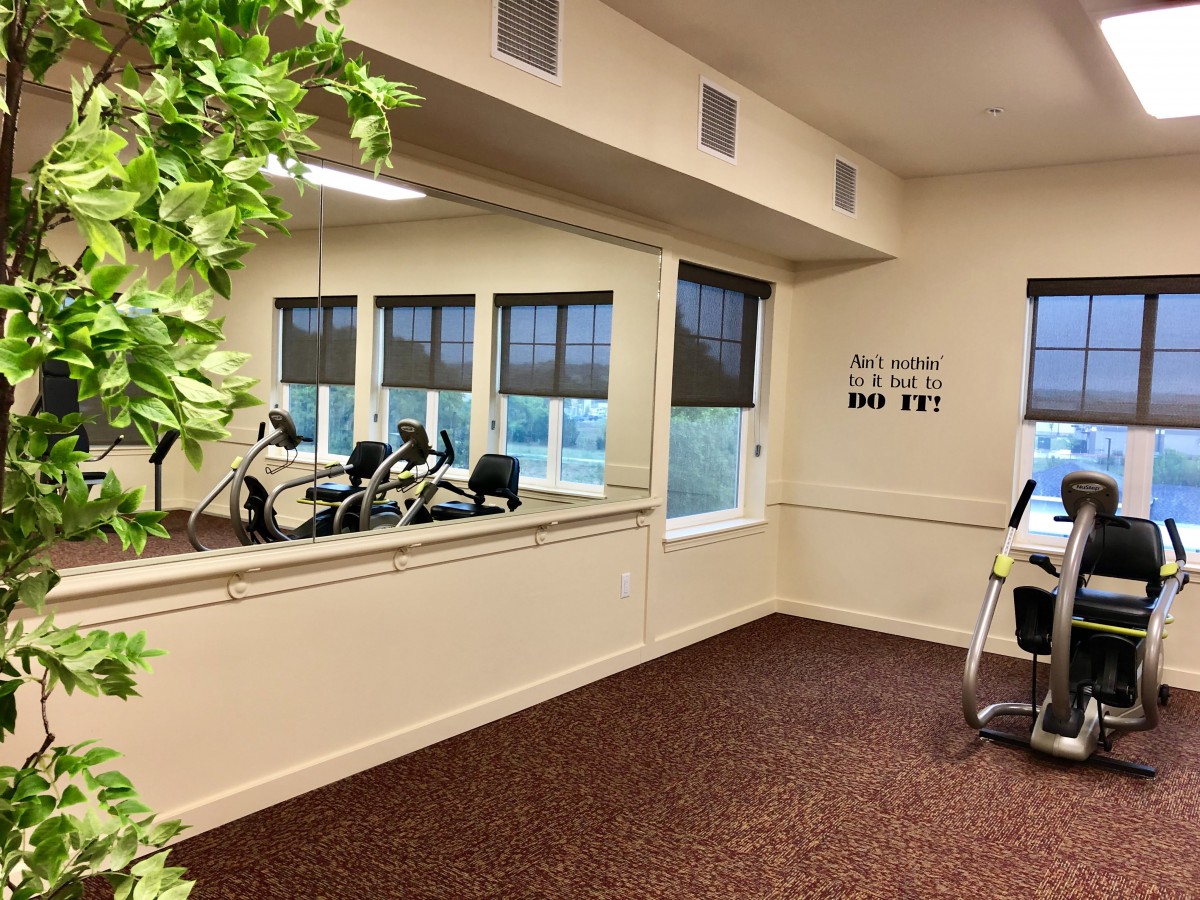 A gym room with exercise bikes, windows, and a large mirror.