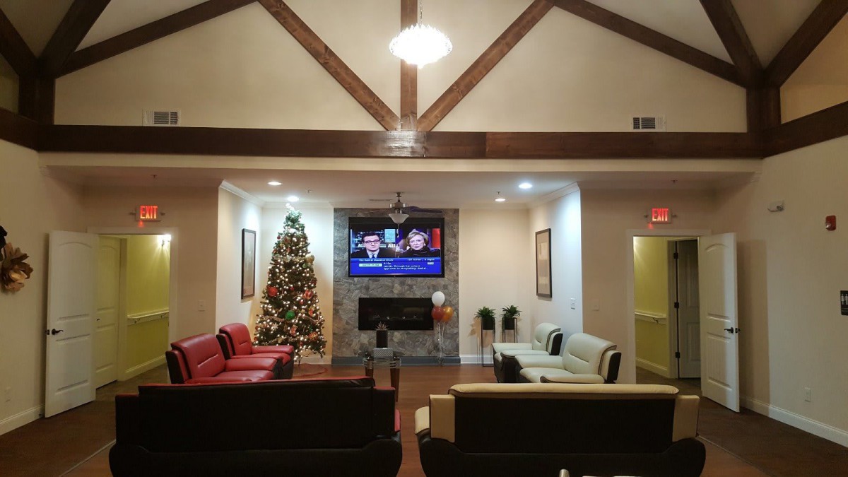 A cozy living room decorated for the holidays with a Christmas tree and a television above the fireplace.