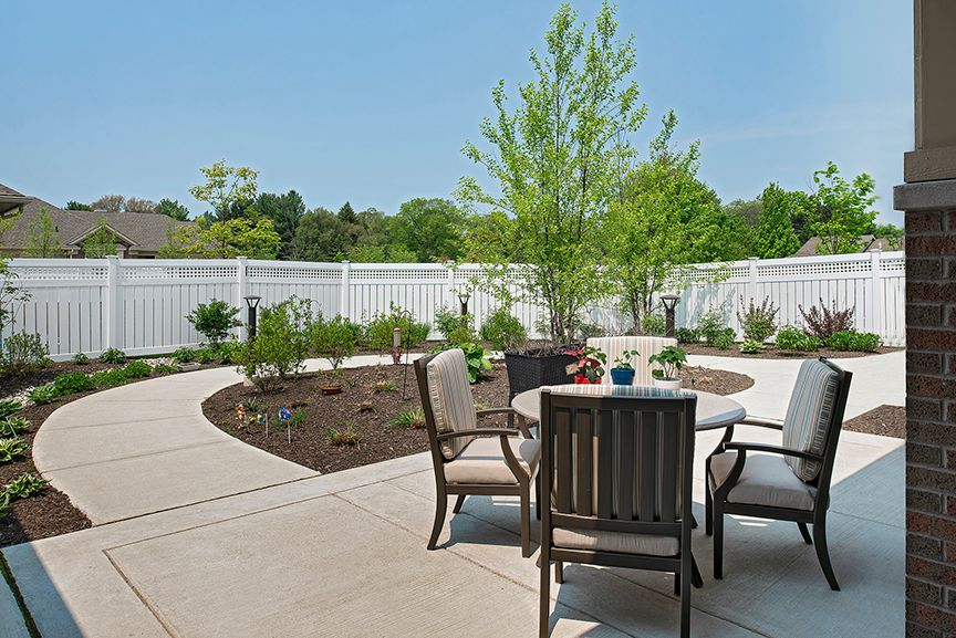 A peaceful outdoor patio area with a round table and chairs, surrounded by a garden and white fence.